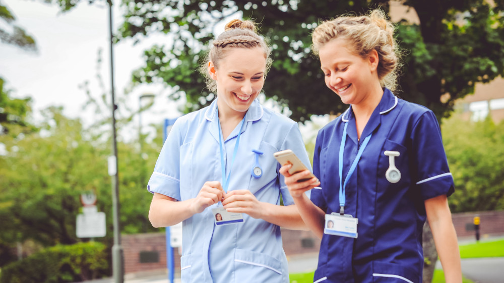 Two young midwives looking at a mobile phone. Photo: Dan Douglas / Superveillance